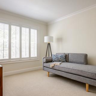 A minimalist living room with a gray sofa, floor lamp, and window shutters.
