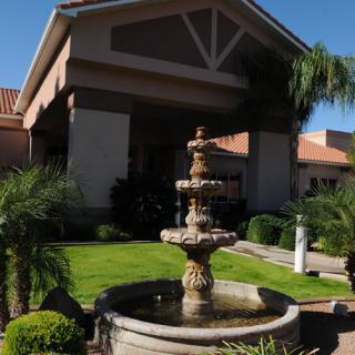 A picturesque fountain in front of a building surrounded by lush greenery and palm trees.