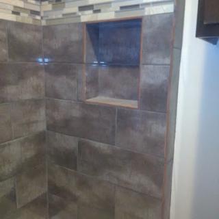 A modern shower featuring stylish tiled walls and a built-in shelf.