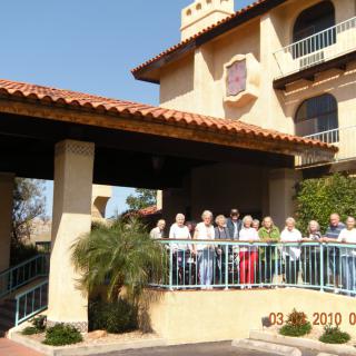 A group of people standing on a balcony in front of a Mediterranean-style building.