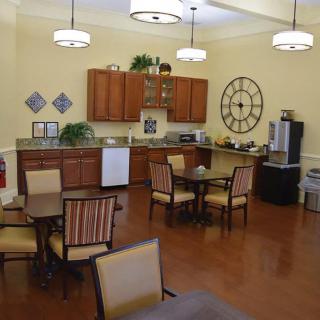 A cozy kitchen and dining area with wooden cabinets, tables, and chairs, featuring a large wall clock and decorative elements.