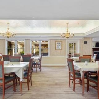 A well-lit dining room with neatly arranged tables and chairs, featuring elegant chandeliers.