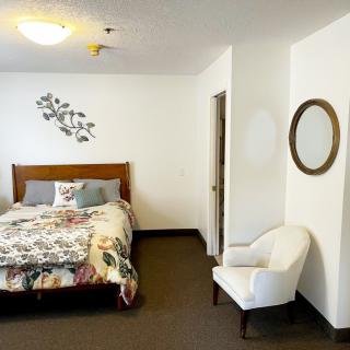 A cozy bedroom featuring a bed with a patterned comforter, an upholstered chair, and a wall-mounted mirror.