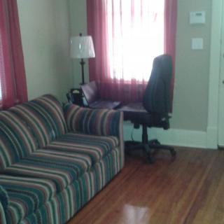 A cozy living room with a striped couch, a desk chair by the window, and wooden floors.