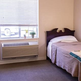 A cozy hotel room with a single bed next to a window and air conditioning unit.