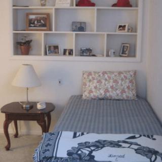 A cozy bedroom with a single bed, decorative shelf, and bedside table.