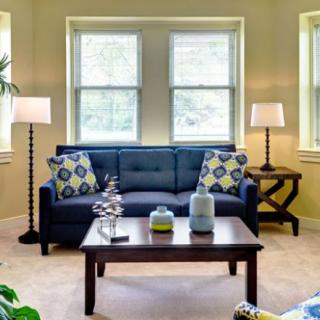 A cozy living room with a blue sofa, decorative cushions, and a wooden coffee table centered between two standing lamps.