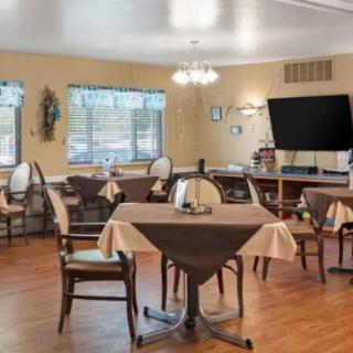 A cozy dining area with multiple tables and chairs, a large television, and natural light coming through the windows.