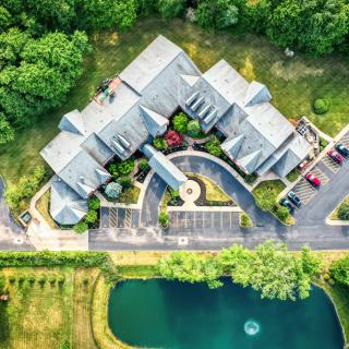 Aerial view of a building with an adjacent parking lot and pond surrounded by trees.