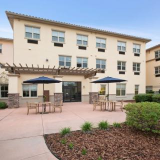 A three-story building with a patio area equipped with tables, chairs, and umbrellas.