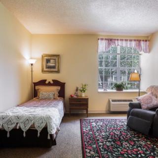 A cozy bedroom with a single bed, armchair, and a large window with pink curtains.