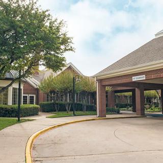 A building entrance with a driveway surrounded by trees and landscaping under a cloudy sky.