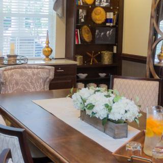 A cozy dining room with a wooden table, adorned with a floral centerpiece and decorative elements on surrounding shelves.