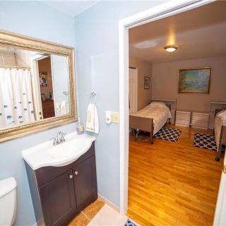 A view from a bathroom into a bedroom with two beds and hardwood flooring.
