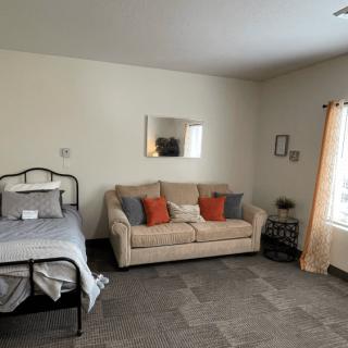 A cozy bedroom with a bed and sofa, decorated with cushions and a wall mirror.