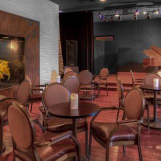 An empty restaurant interior with brown chairs and round tables, featuring a small stage area.