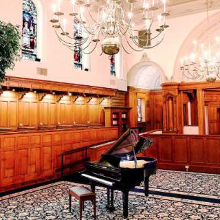 A grand piano in an elegant room with wooden paneling and stained glass windows.