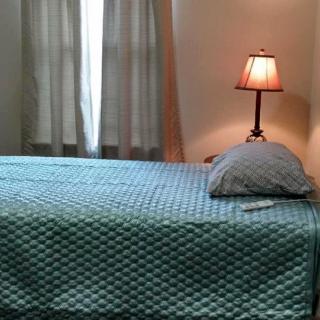 A neatly made bed with a textured blue coverlet beside a lit lamp.