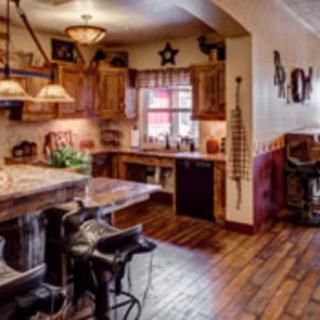 A rustic kitchen interior featuring wooden cabinets, bar stools resembling saddles, pendant lighting, and various decorative elements.