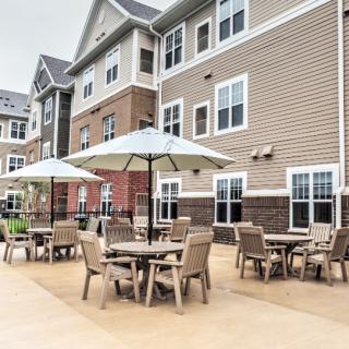A well-furnished outdoor patio area with tables, chairs, and umbrellas in front of an apartment building.