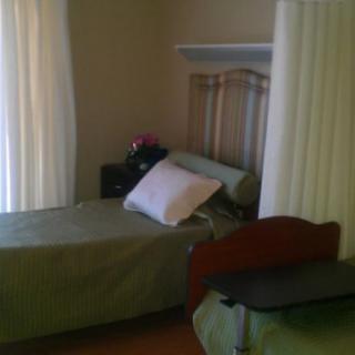 A simple bedroom with a bed next to a window, featuring curtains and a nightstand.