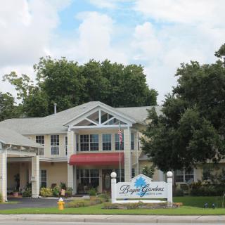 A two-story building with a red awning and a sign that reads 'Bay Pointe' in front, surrounded by trees and under a partly cloudy sky.