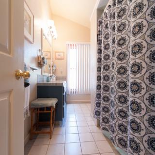 A well-lit bathroom featuring a patterned shower curtain, vanity with mirror, and tiled flooring.