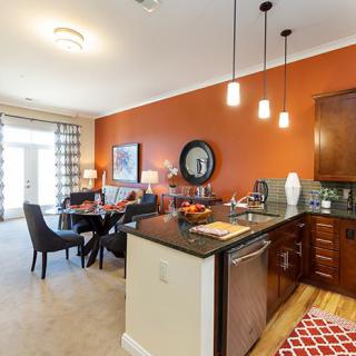 A modern open-concept kitchen and dining area with vibrant orange walls and stylish pendant lighting.