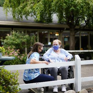 A caregiver engages in a warm conversation with a woman in a wheelchair outdoors, highlighting the importance of social connections in healthcare.