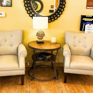 A cozy living room setup featuring two beige armchairs, a round table with a lamp, and a decorative mirror on the wall.