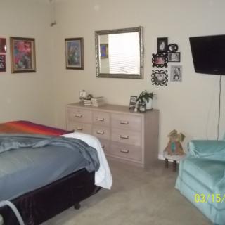 A cozy bedroom with a bed, dresser, mirror, and wall-mounted TV.