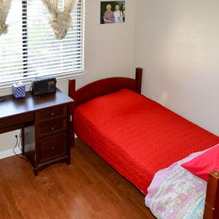 A tidy bedroom with a red bedspread and a wooden desk by the window.