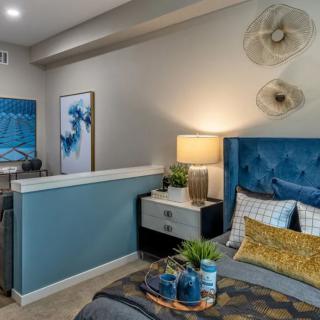 A modern bedroom featuring a blue and gray color scheme with decorative artwork, a plush bed, and ambient lighting.
