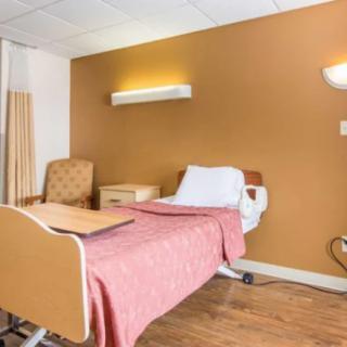 A hospital room with a bed and chair, featuring a warm color scheme.