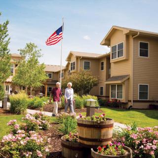A serene residential area featuring a well-maintained garden and an American flag, with two people walking along the path.