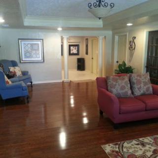 A spacious and elegantly decorated living room featuring a cozy red sofa, a blue armchair, and warm wooden flooring.