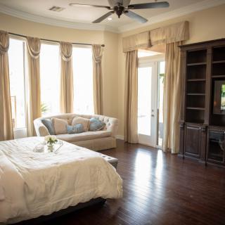 A cozy bedroom featuring a bed, sofa, and large windows with elegant curtains.
