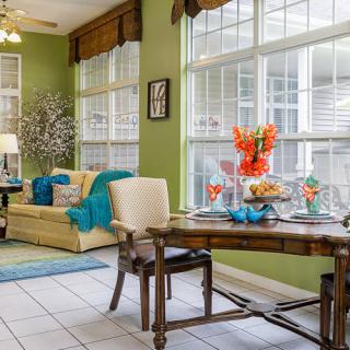 A cozy living and dining area with large windows, adorned with colorful decor and comfortable furniture.