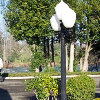 A peaceful park scene with a lamp post, lush trees, and a flowing river in the background.