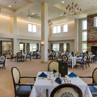 An elegant restaurant dining room with neatly arranged tables and chairs, featuring large windows and a chandelier.