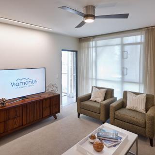 A modern living room with comfortable armchairs, a television, and a ceiling fan.