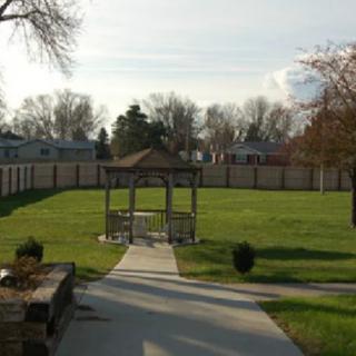 A quaint park with a gazebo, surrounded by a grassy area and enclosed by a wooden fence.
