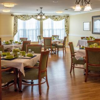 A well-appointed dining room with neatly arranged tables and chairs, featuring elegant decor and large windows with curtains.