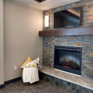 A modern living room featuring a cozy fireplace with a mounted TV above, accented by a stone wall, pillow, and blanket.