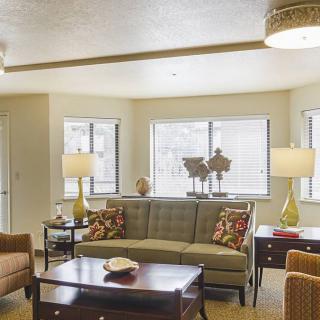 A cozy living room with a sofa, armchairs, lamps, and coffee table near large windows.
