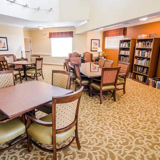 A cozy library with multiple tables and chairs, surrounded by bookshelves in a well-lit community room.
