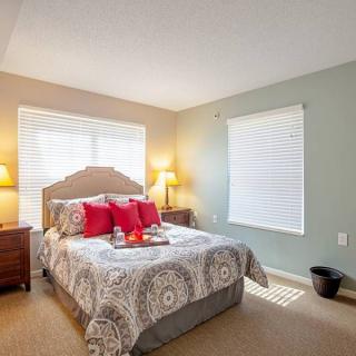 A cozy bedroom interior featuring a neatly made bed with patterned bedding, red accent pillows, and warm lighting from bedside lamps.