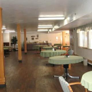 An empty dining room with tables and chairs, well-lit by overhead lights and natural light from windows.