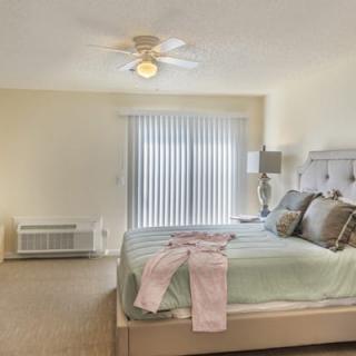 A cozy bedroom with a neatly made bed, ceiling fan, and soft lighting.