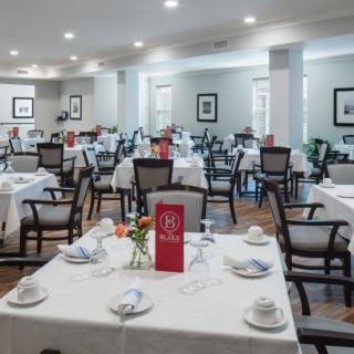 An elegant dining room setup with neatly arranged tables and chairs, featuring white tablecloths.